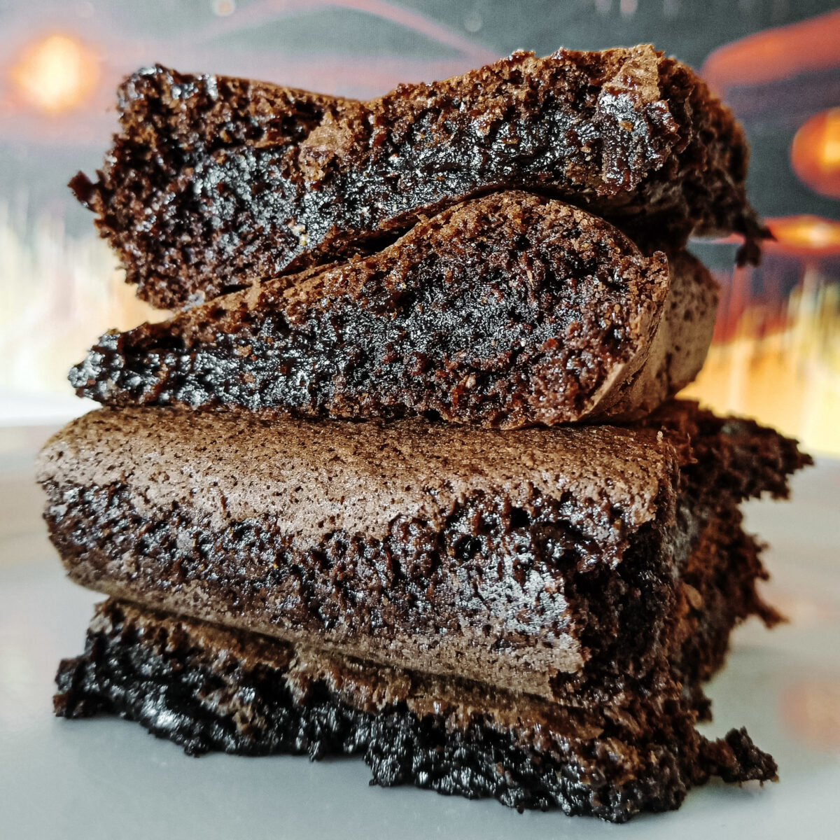 Old-fashioned fudgy brownies in front of an orange painting.