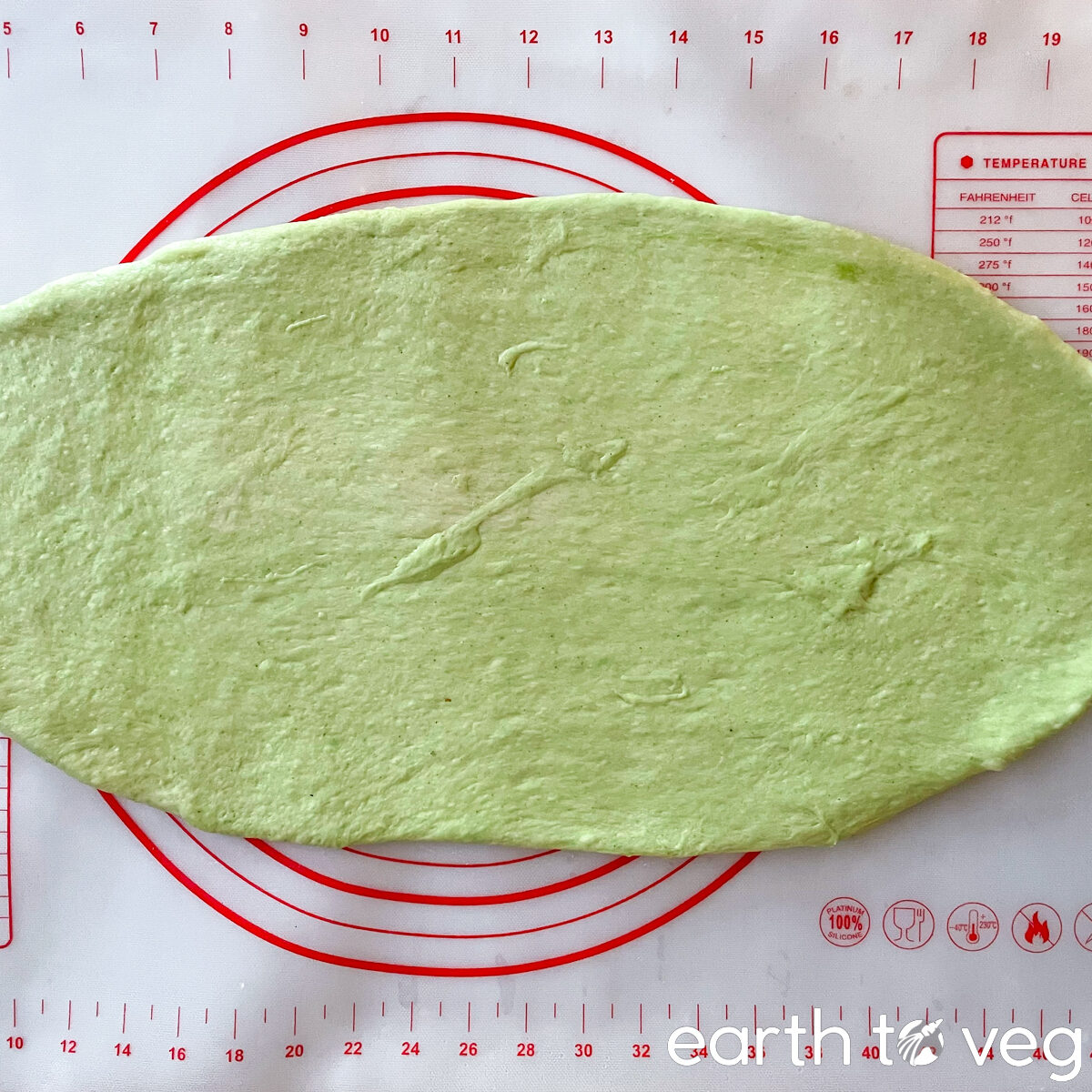 The pandan bread dough is rolled out into a thin sheet on a silicon pastry mat.
