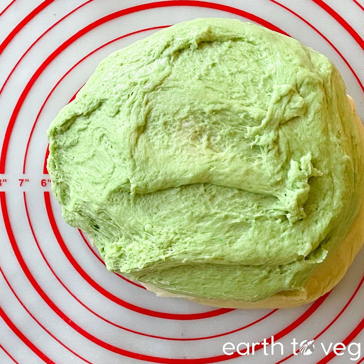 A ball of kneaded green dough rests on a silicon mat.