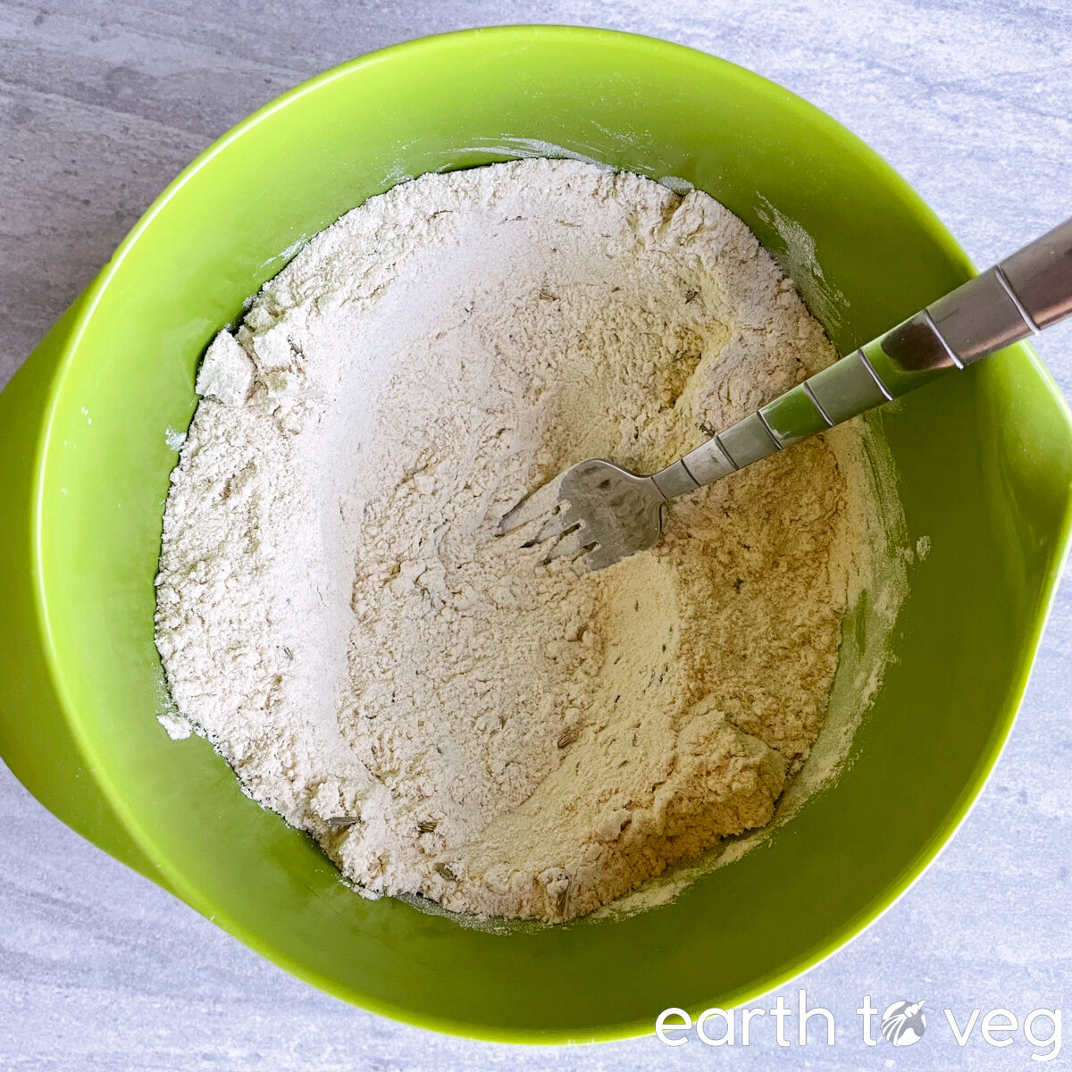 Dry ingredients for Irish soda bread are mixed together with a metal fork in a green bowl.