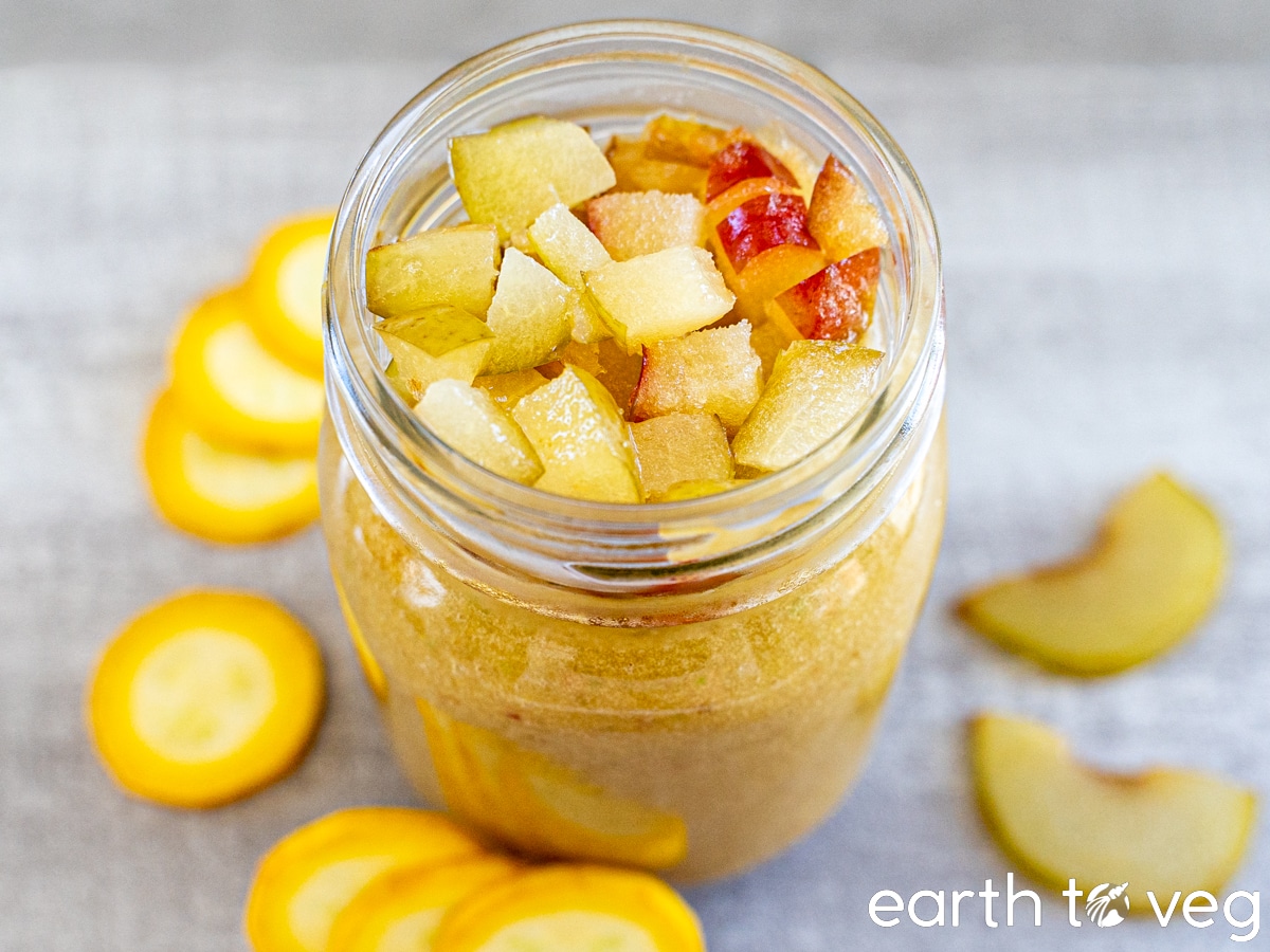 A glass of zucchini smoothie on a grey counter, surrounded by slices of yellow zucchini and peaches.