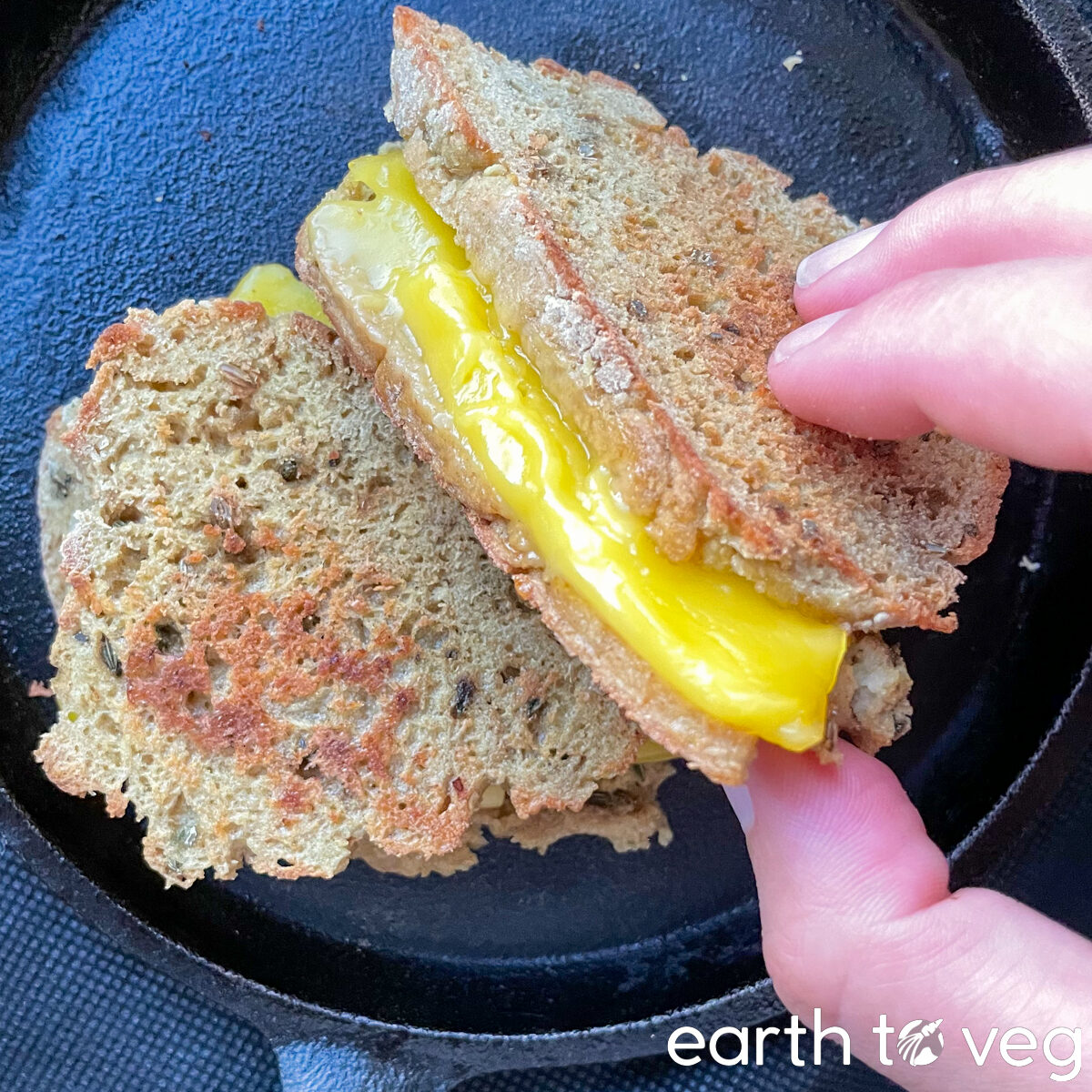 hand holding a sliced cross section of a vegan grilled cheese sandwich in a small cast iron pan