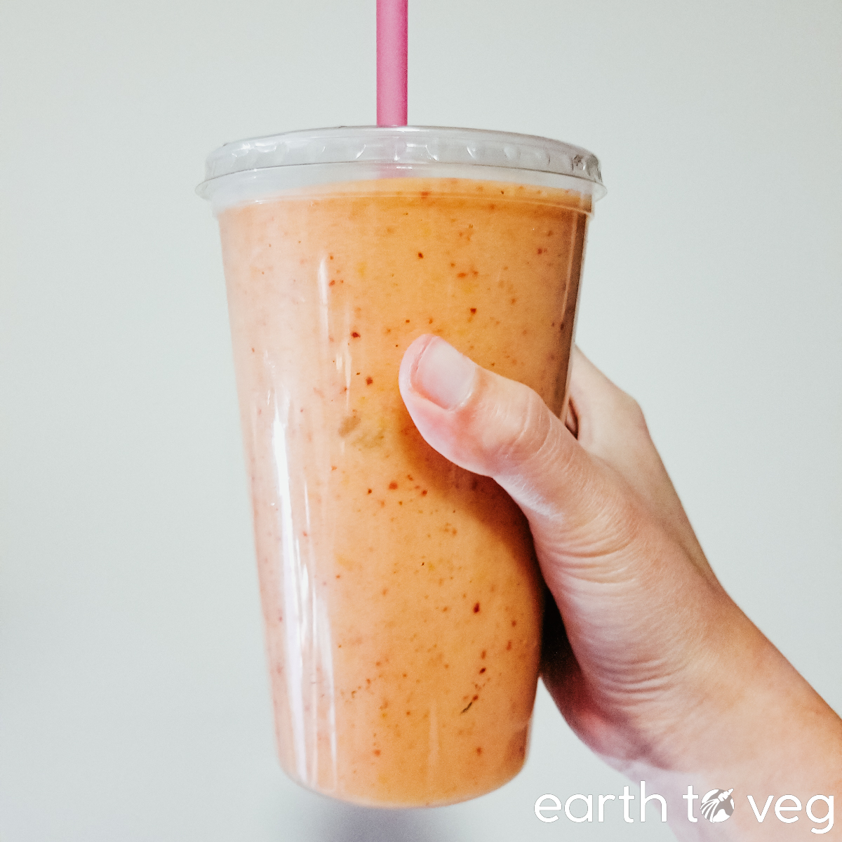 A hand holds up a plastic tumbler full of vibrant orange smoothie.