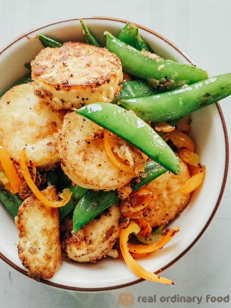 A top-down view of a bowl of crunchy soft tofu with sugar snap peas and orange bell pepper.
