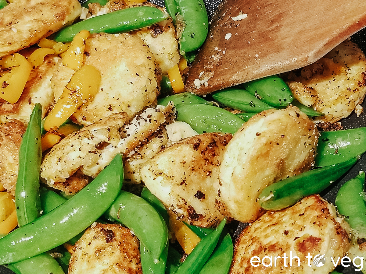 A closeup shot of a wooden spatula stir frying snap peas and fried tofu together.