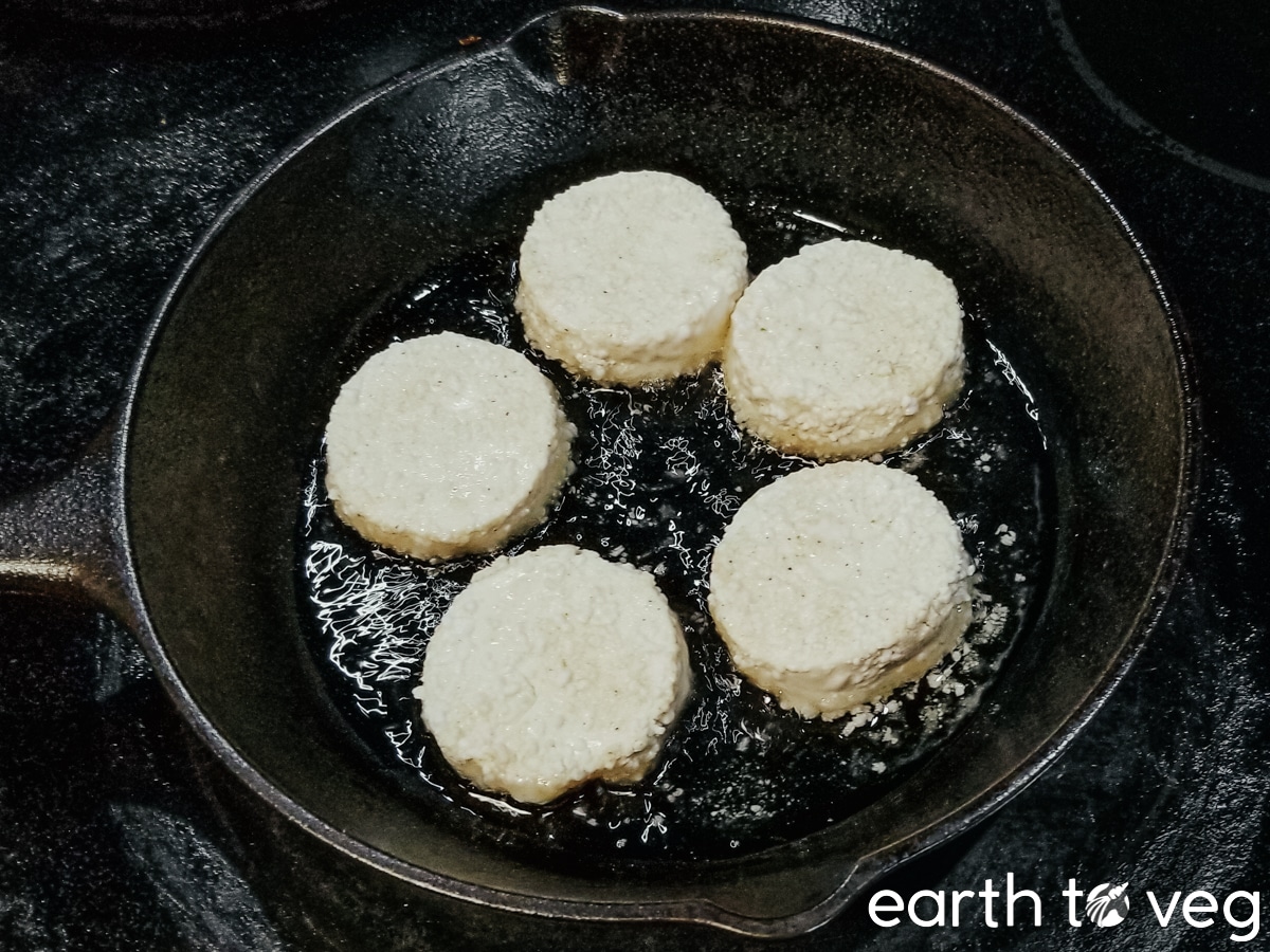 Five slices of cornstarch-coated silken tofu being fried in a small cast iron skillet.