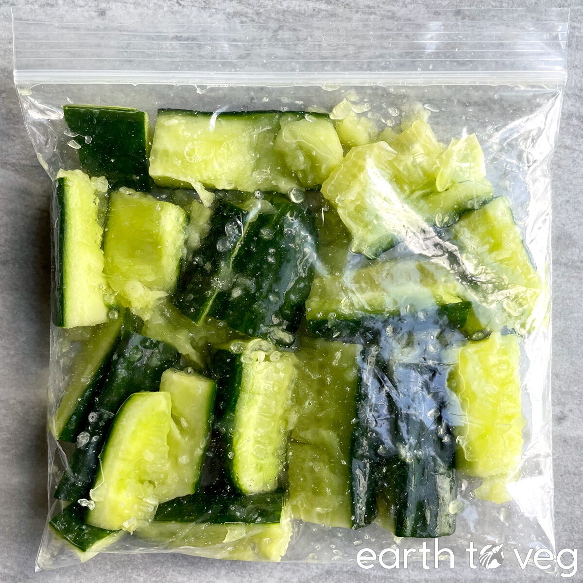 Smashed cucumbers in a small ziploc bag on a grey counter.