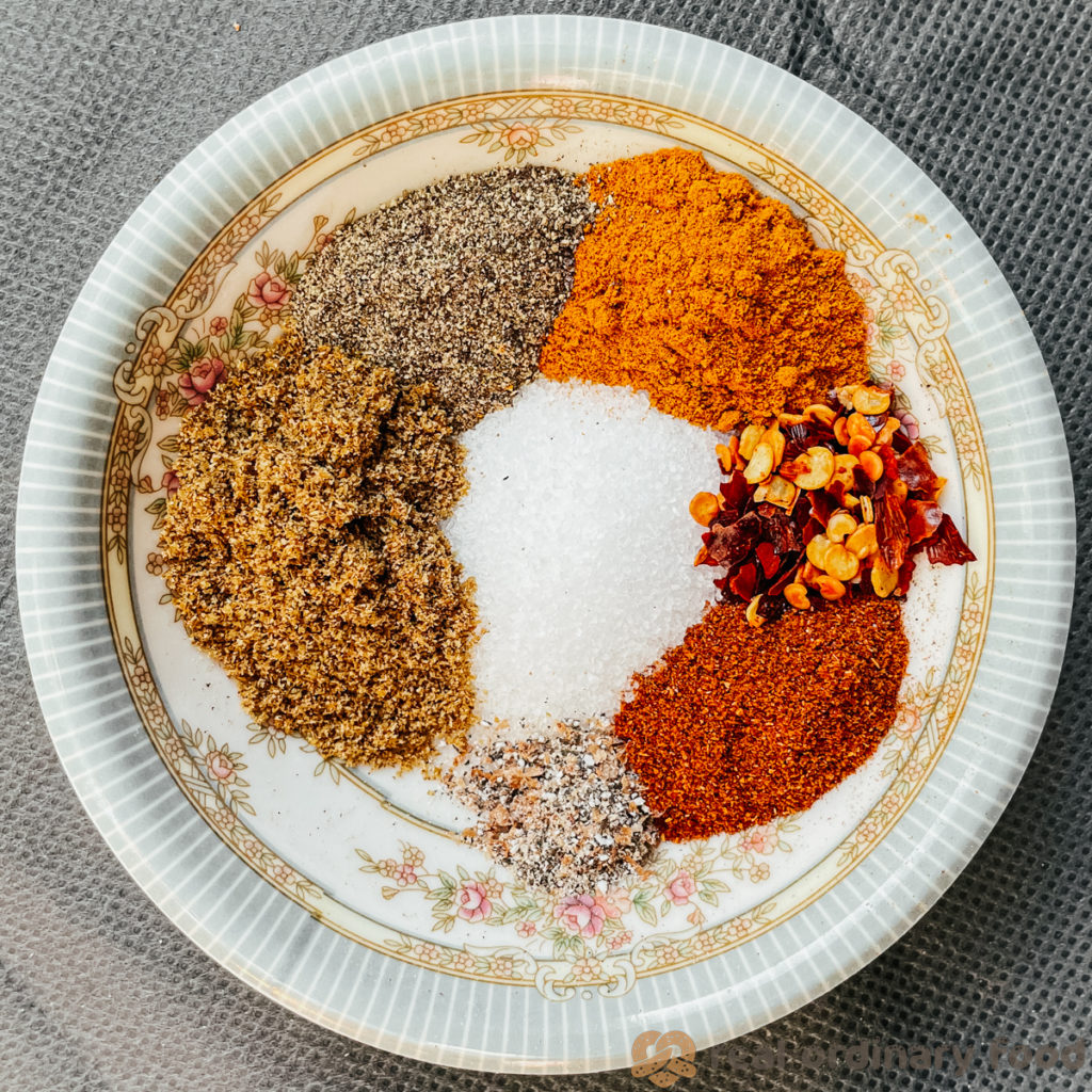 The spices for borani banjan are laid out on a small saucer on a grey tablecloth.