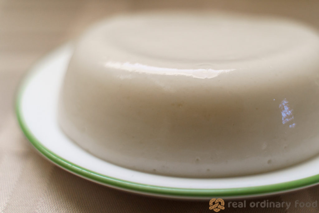 A pale, white, jiggly-looking plate of mahalabia rice pudding on a beige tablecloth.