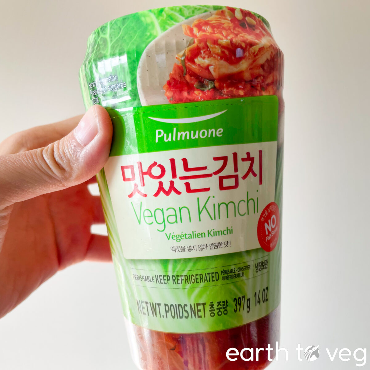 A hand holds up a small plastic jar of vegan kimchi.