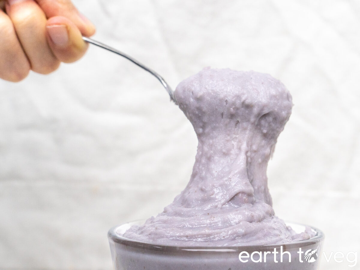 A hand holding a spoon scooping up thick, thick taro paste.