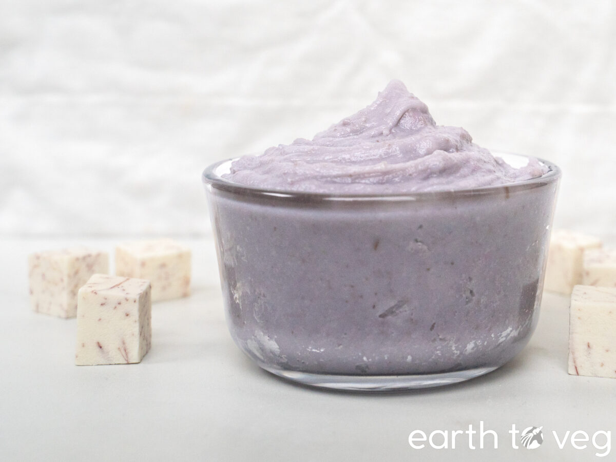 A glass container filled to the brim with blended taro paste sits on a white countertop.