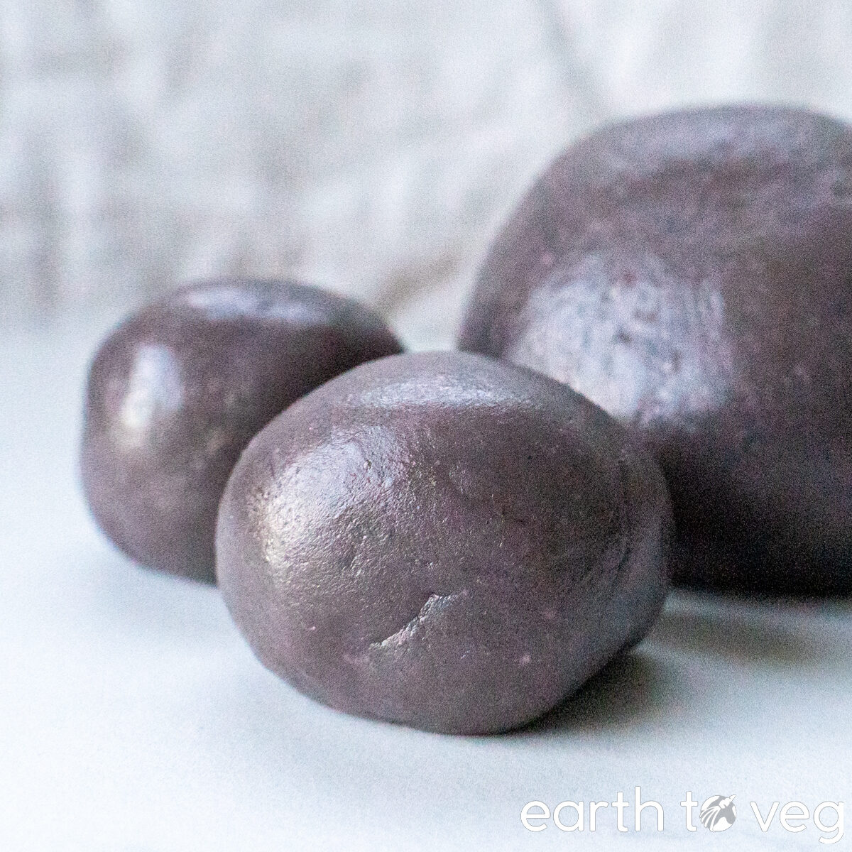 Thickened taro paste is rolled into three balls of varying size on a white countertop.