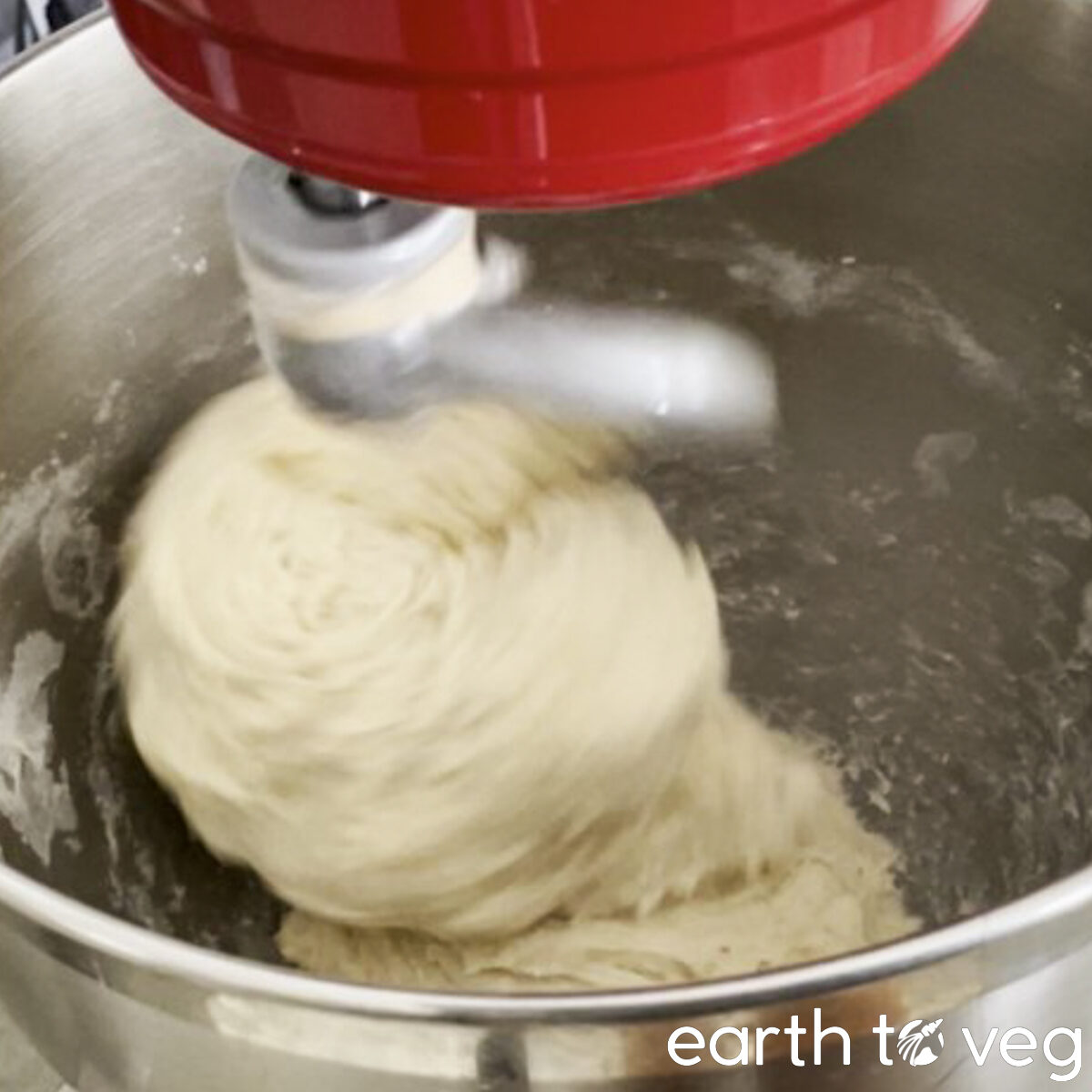 A shaggy ball of hot water dough is kneaded against the walls of a metal stand mixer bowl.