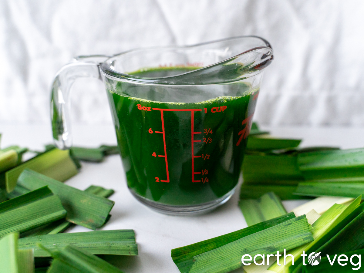 Homemade pandan juice in a glass cup surrounded by chopped fresh pandan.
