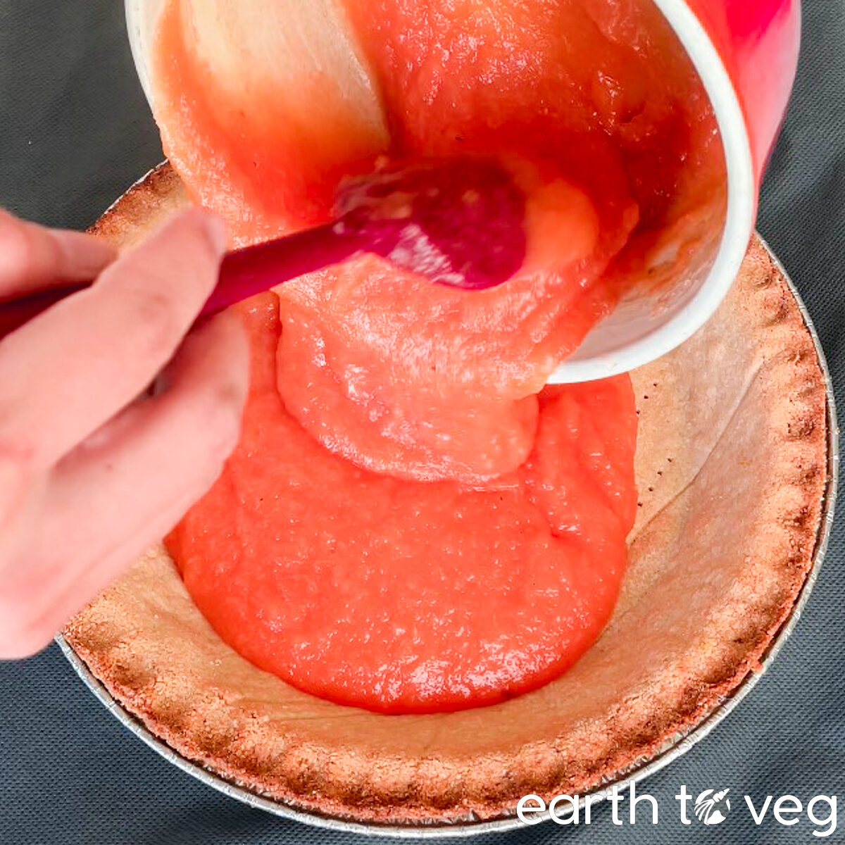 Pink pineapple pie filling is poured into a pre-baked pie shell.