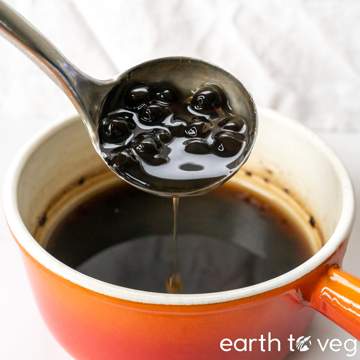 A metal scoop full of cooked brown tapioca pearls.