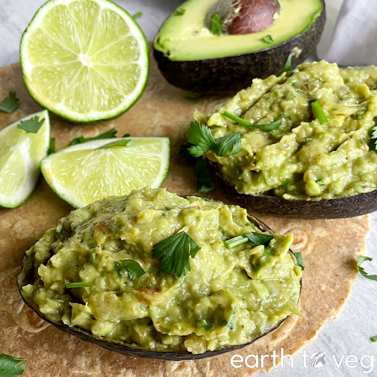 two avocado halves are filled with guacamole, with limes in the background.