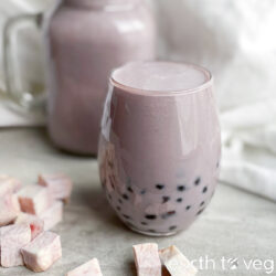 A glass of homemade taro boba tea on a grey countertop with cubed taro pieces.