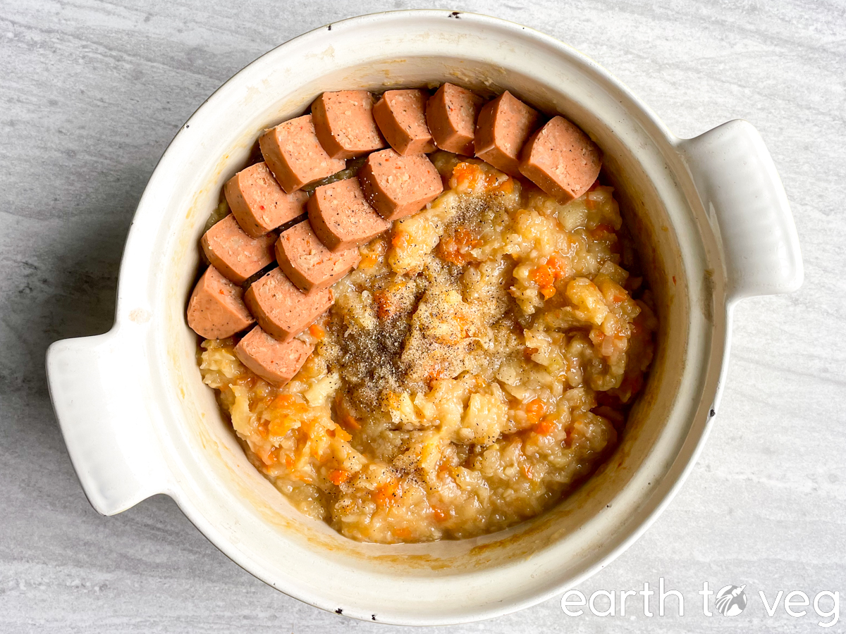 A Dutch oven full of hutspot with sausage on a grey tabletop.