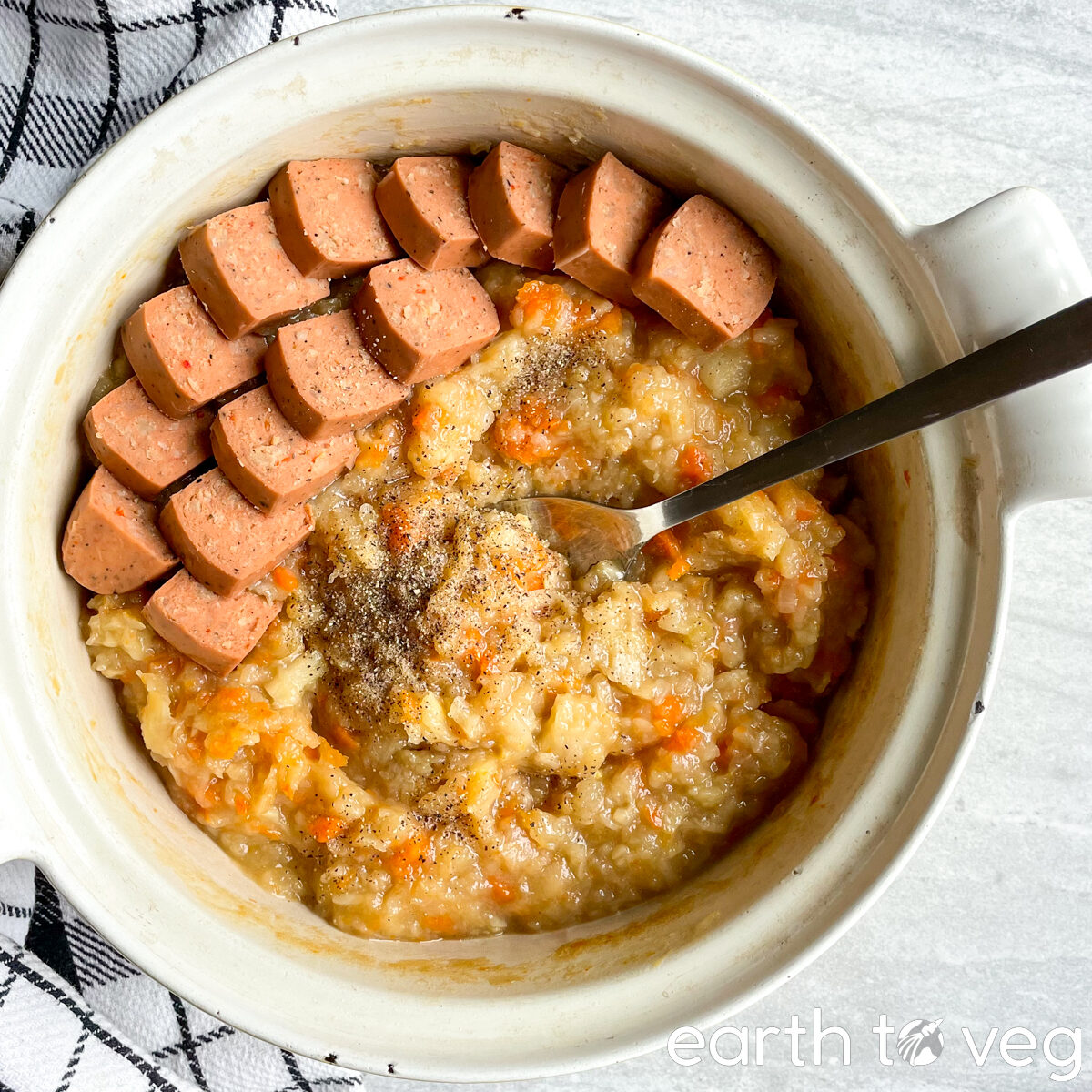 Metal spoon scooping from a Dutch oven filled with hutspot and veggie sausage.