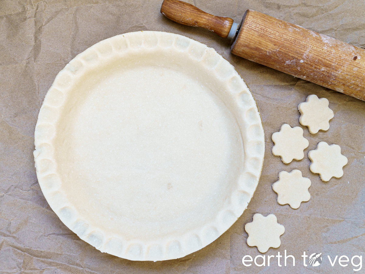 unbaked shortening pie dough with rolling pin and flower-shaped crust cut outs on the side