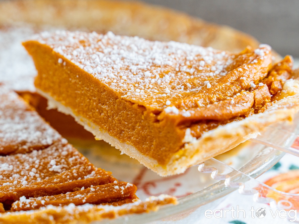 A slice of coconut milk pumpkin pie is sliced and lifted out of the pie pan.