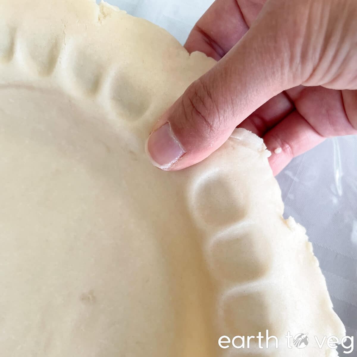 A thumb presses down on the edges of the rolled pie dough to form a dimpling pattern.