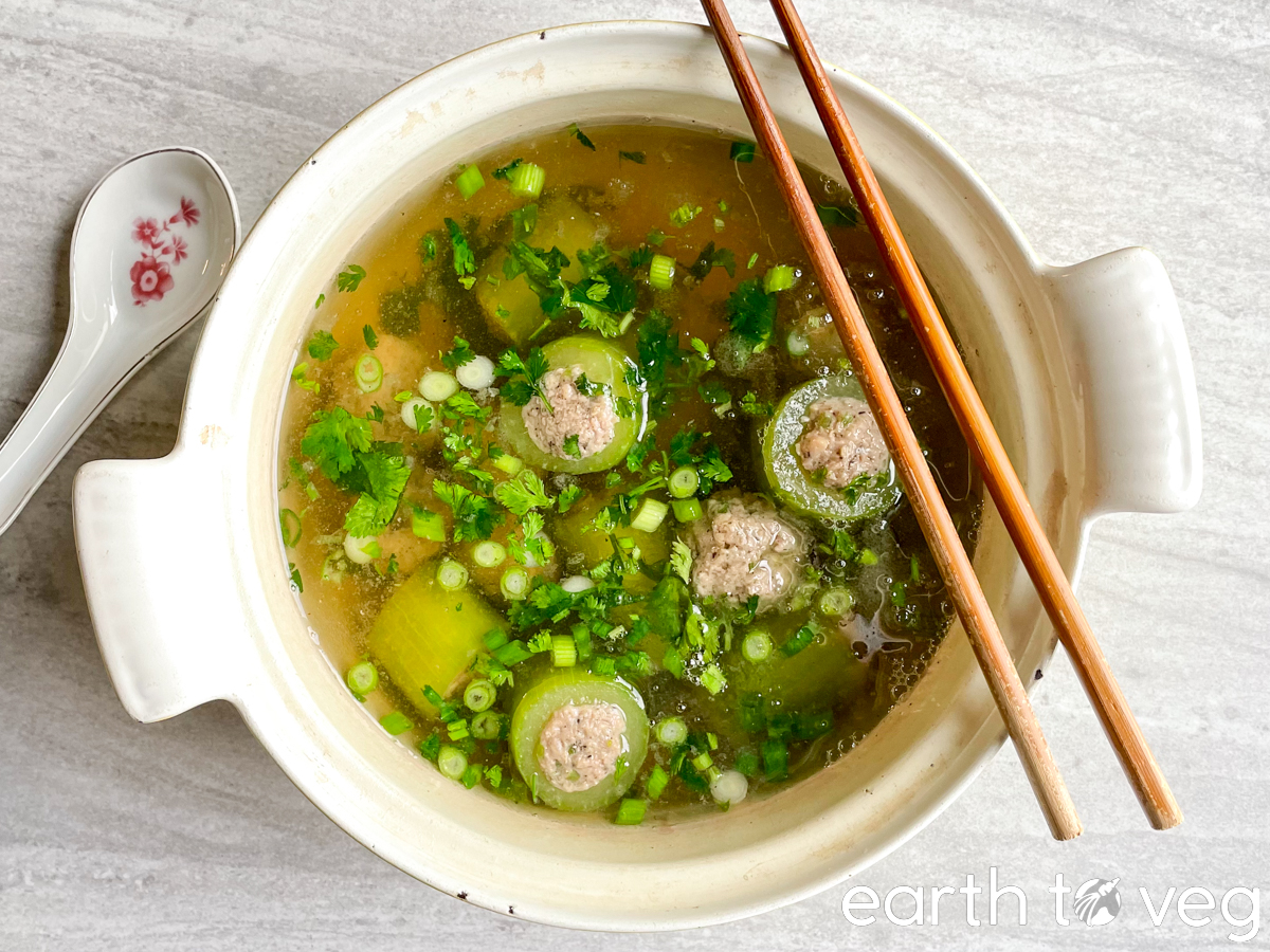 chopsticks and porcelain soup spoon arranged next to a large pot of Thai stuffed cucumber soup