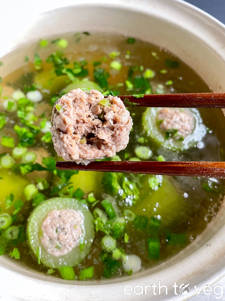 wooden chopsticks holding up a beyond beef meatball with a bite taken out of it