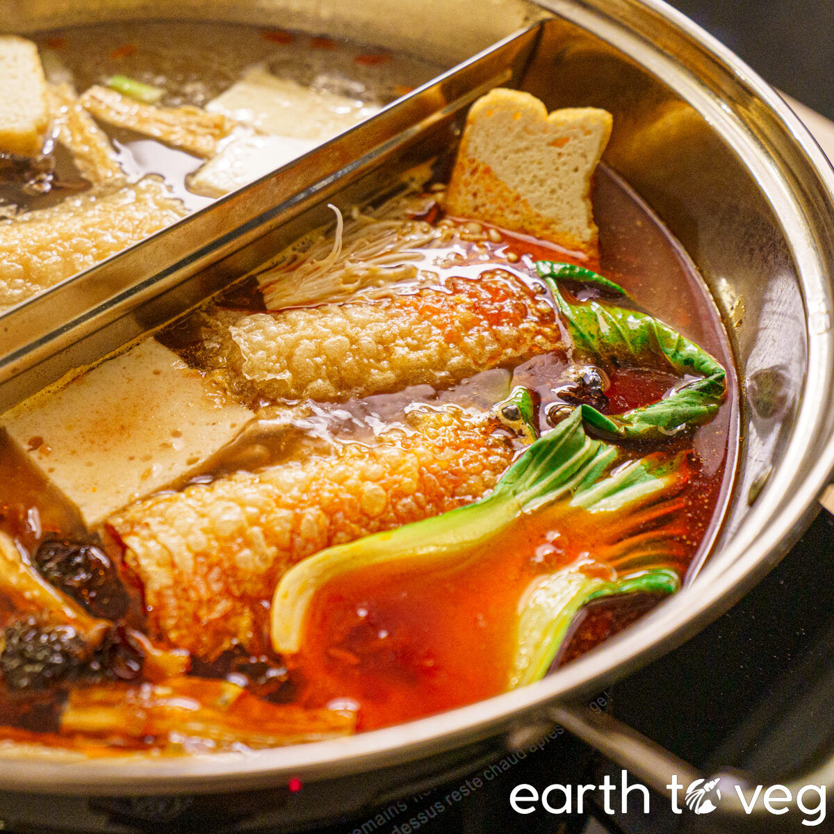 simmering spicy red chinese hot pot broth filled with tofu, bok choy, soy rolls, fried bean curd, and wood ear mushrooms