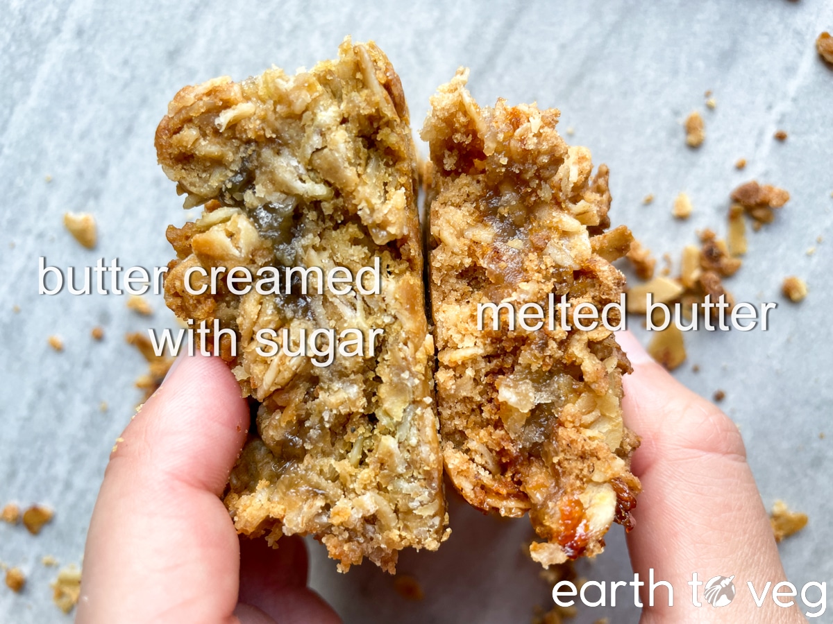 A hand holds up two slices of hjónabandssæla cake to show the side-by-side comparison of the cross section.