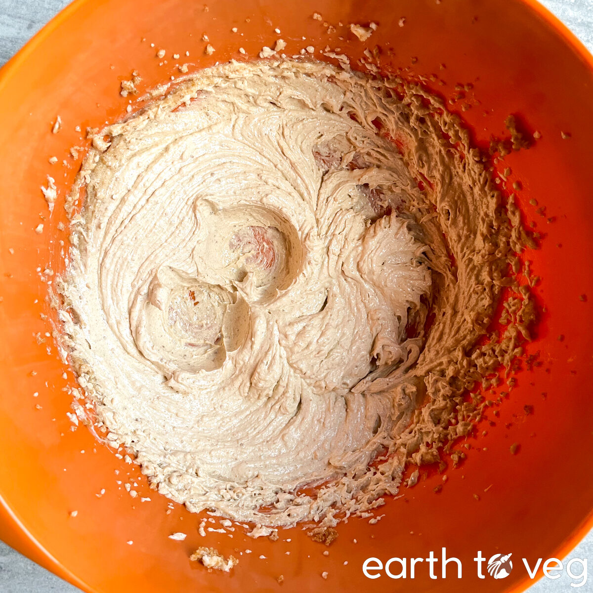 Brown sugar and vegan butter are creamed together in an orange melamine mixing bowl.