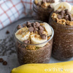 Chocolate banana chia pudding in a glass cup on a grey counter in front of a checkered white cloth.