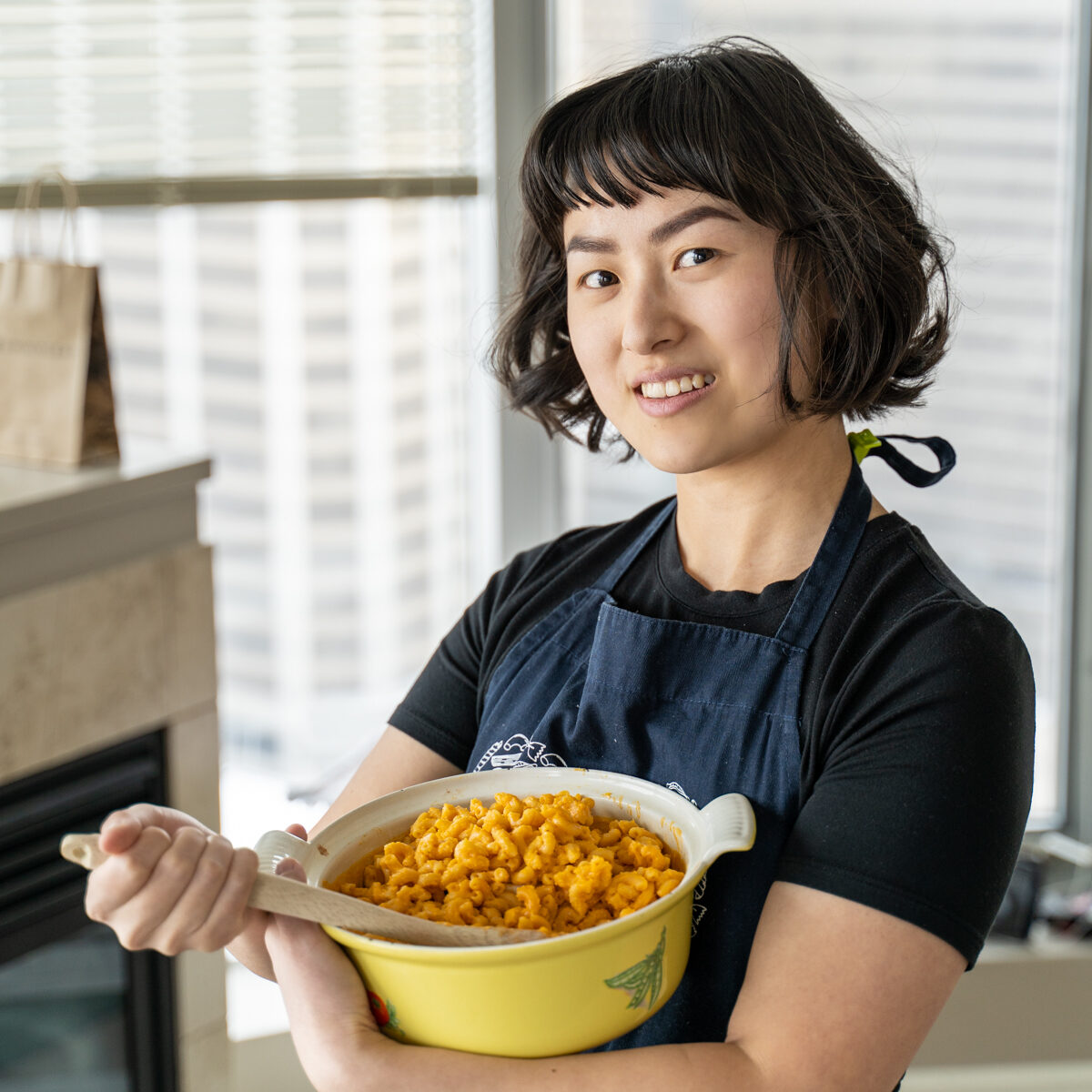 Young Asian woman holds a Dutch oven full of vegan macaroni and cheese.