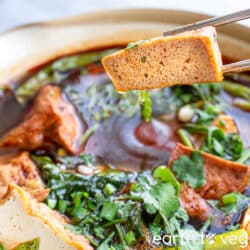 Chopsticks holding stewed stinky tofu over a pot of soup.