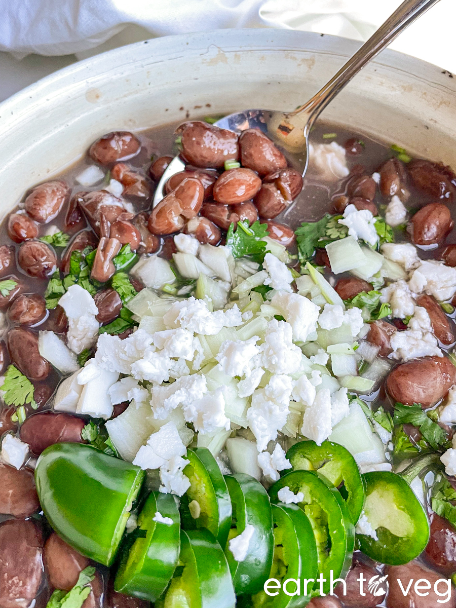 A spoon dips and scoops out a helping of frijoles from a pot full of beans.