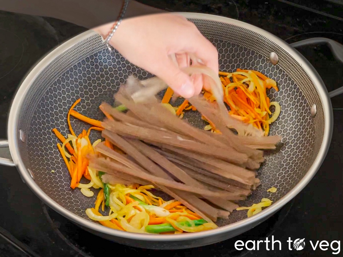 The soaked sweet potato noodles are added to the wok.
