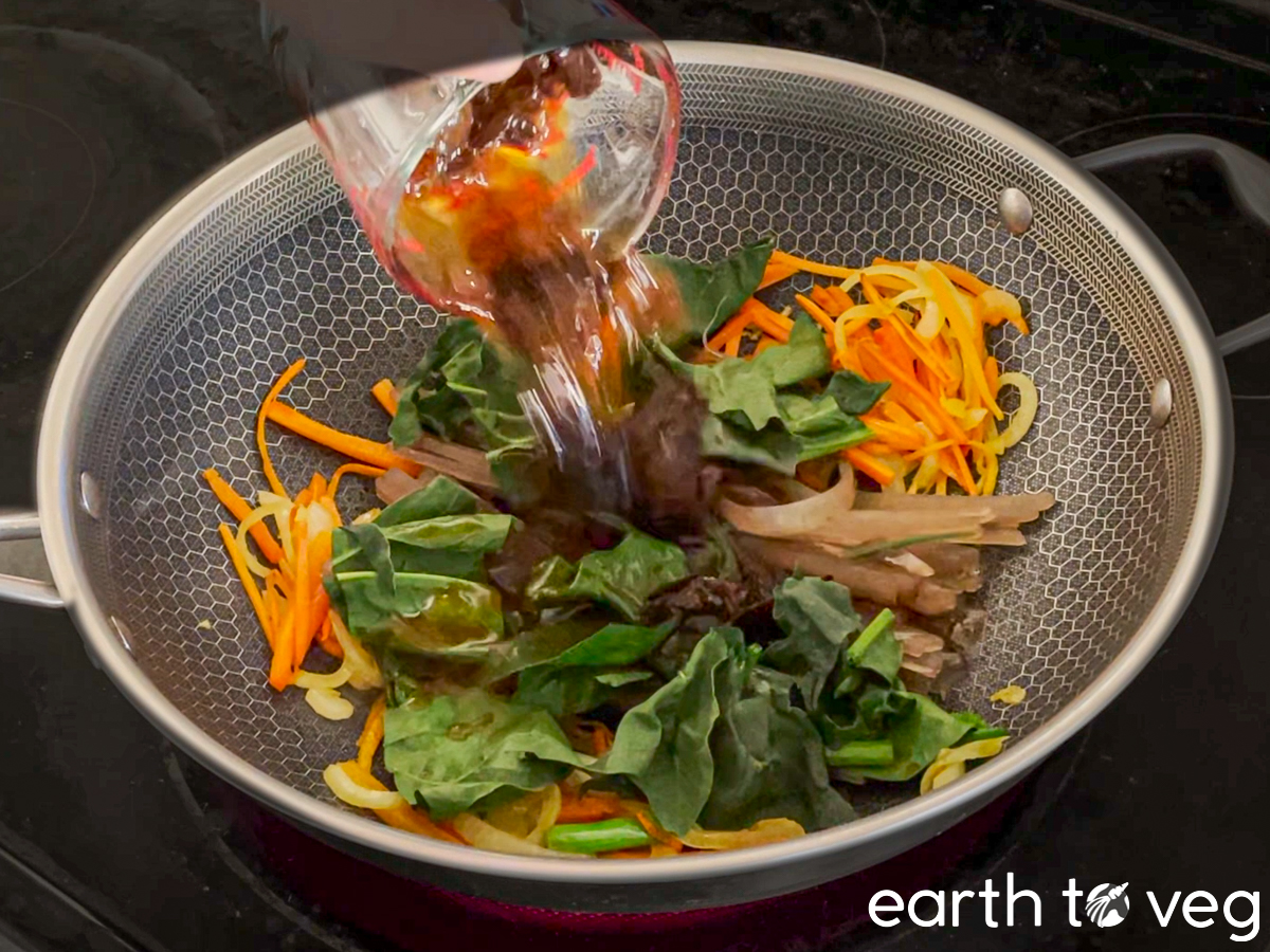 The japchae sauce mixture gets poured over the wok ingredients.