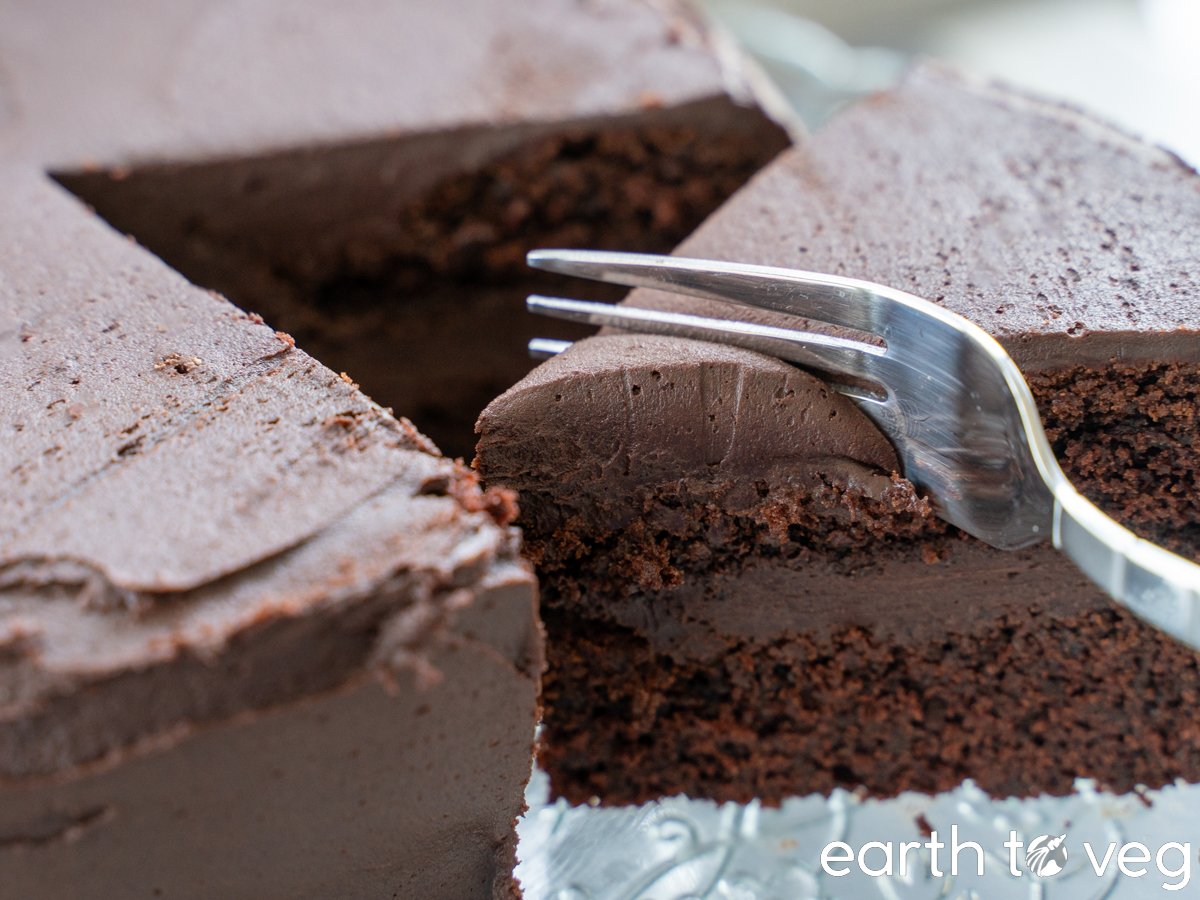 A metal fork carving into a double-layer chocolate frosted chocolate blender cake.