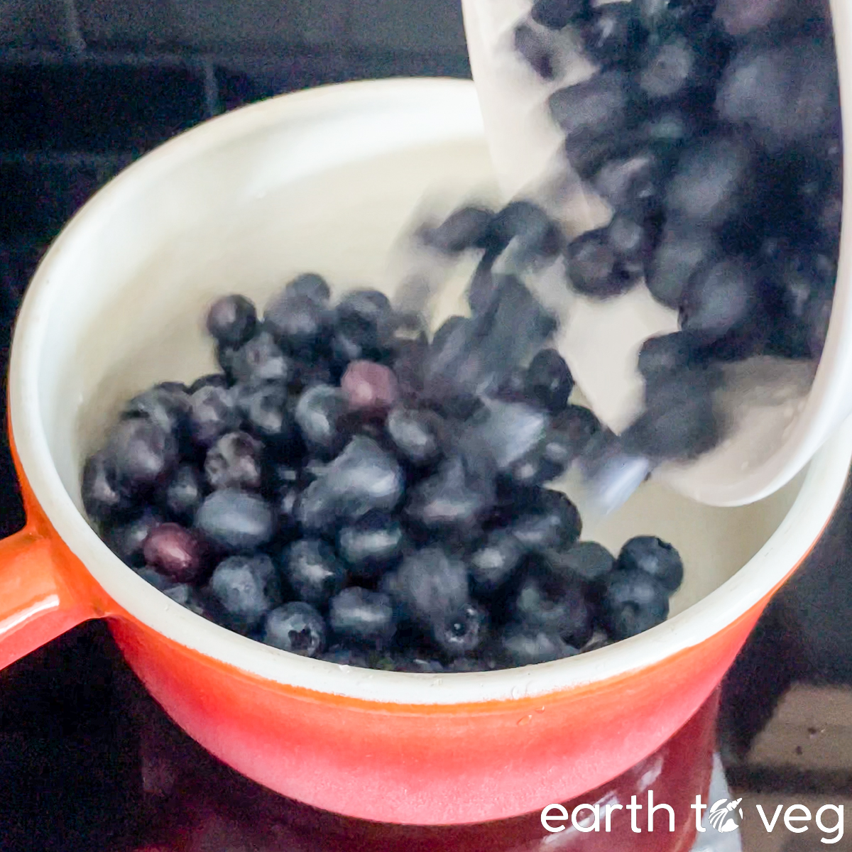 Fresh blueberries are poured into an orange enamel pot.