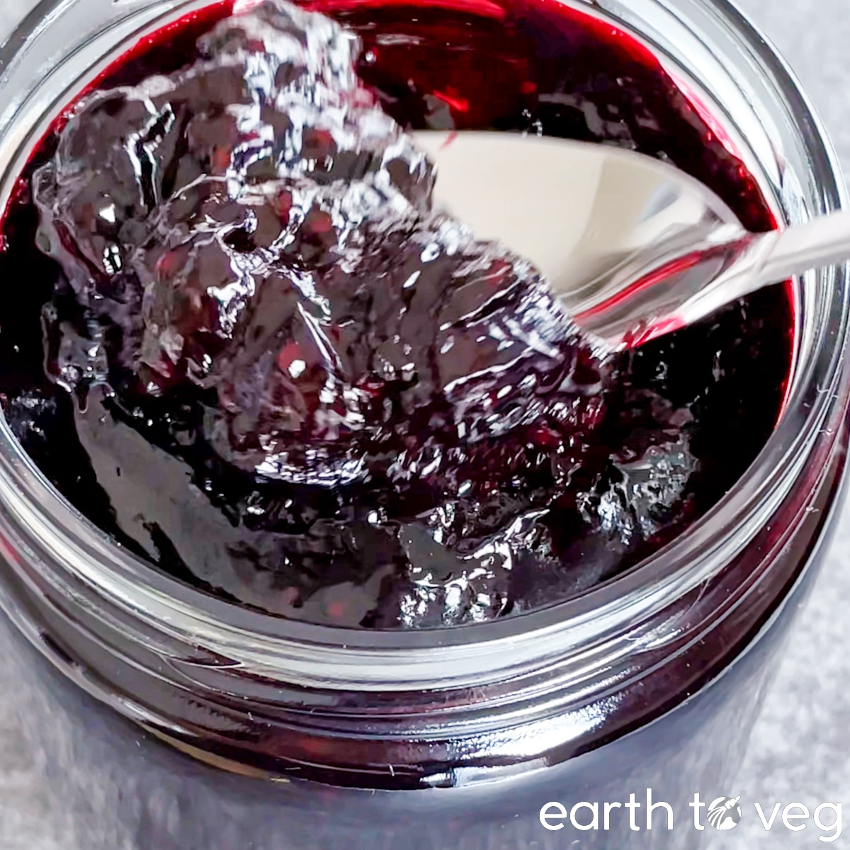 Haskap jam being scooped out of a glass jar with a metal spoon.