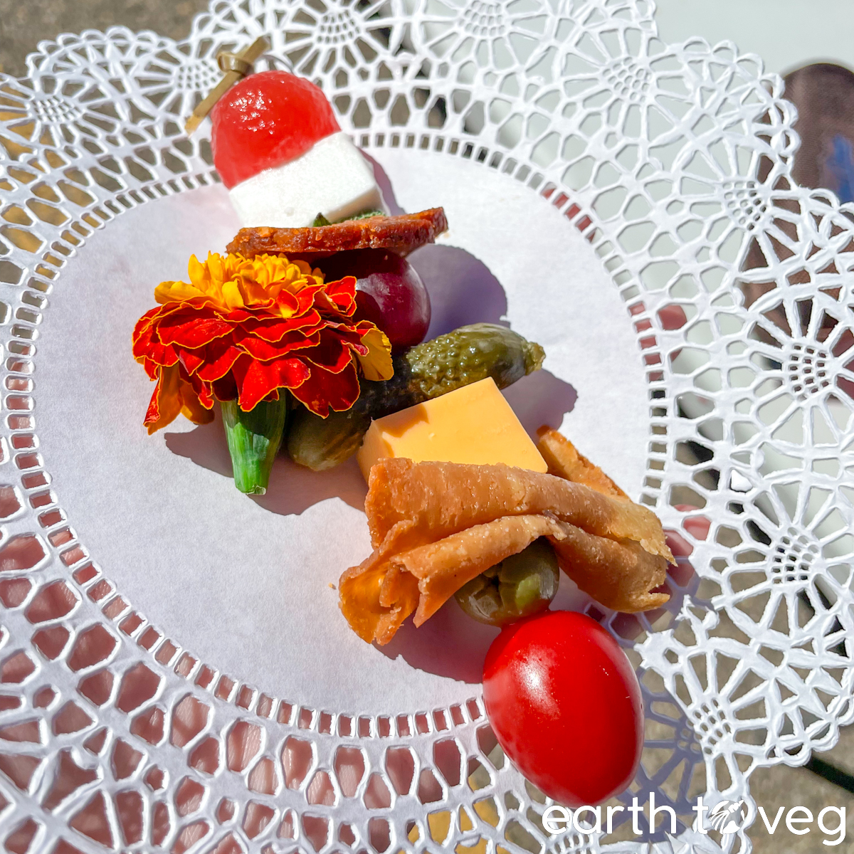 A skewer of vegan cheese, charcuterie, and fresh tomatoes resting on a paper doily.
