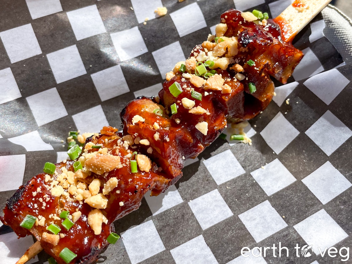 A small skewer of saucy seitan skewers coated in sweet teriyaki sauce on checkered wax paper.