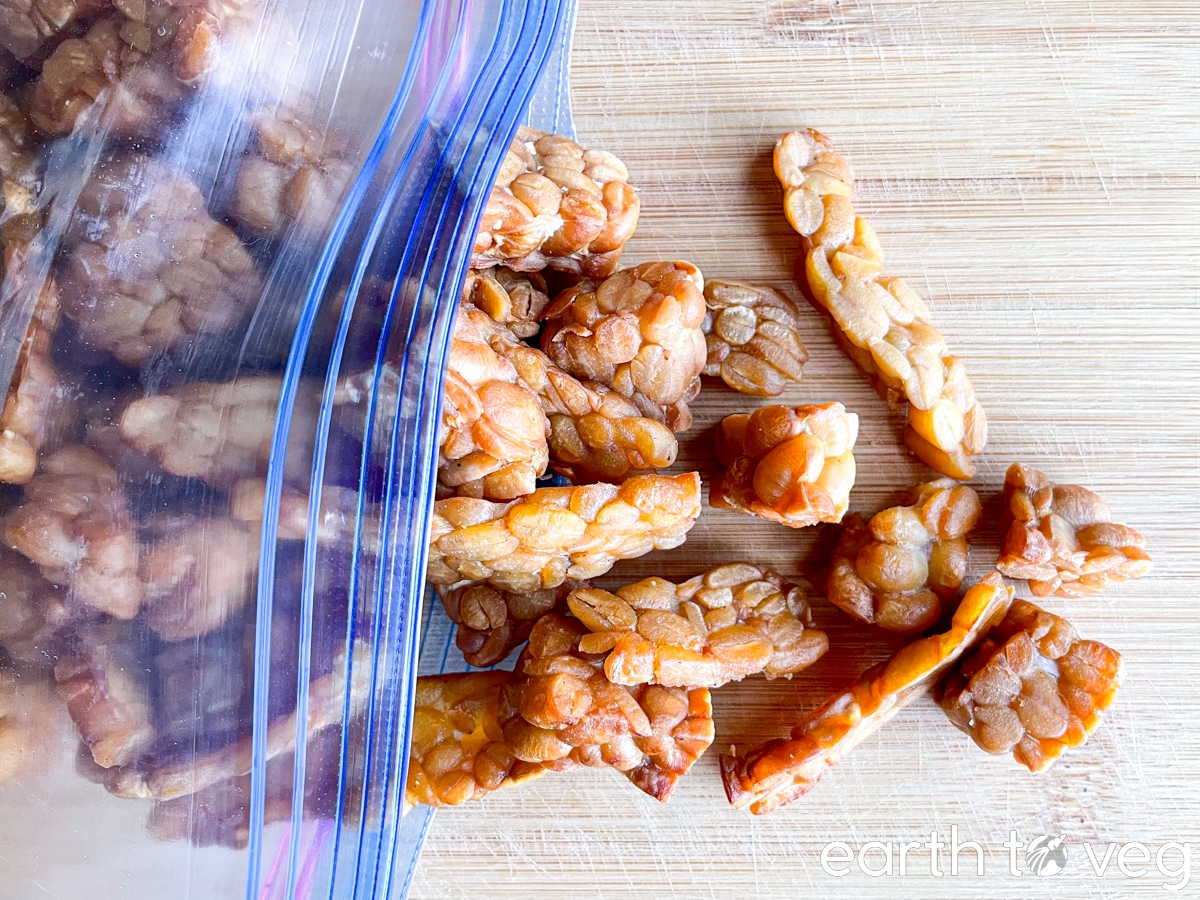 Homemade traditional Indonesian-style fried tempeh strips scattered out of a ziploc bag onto a wooden cutting board.