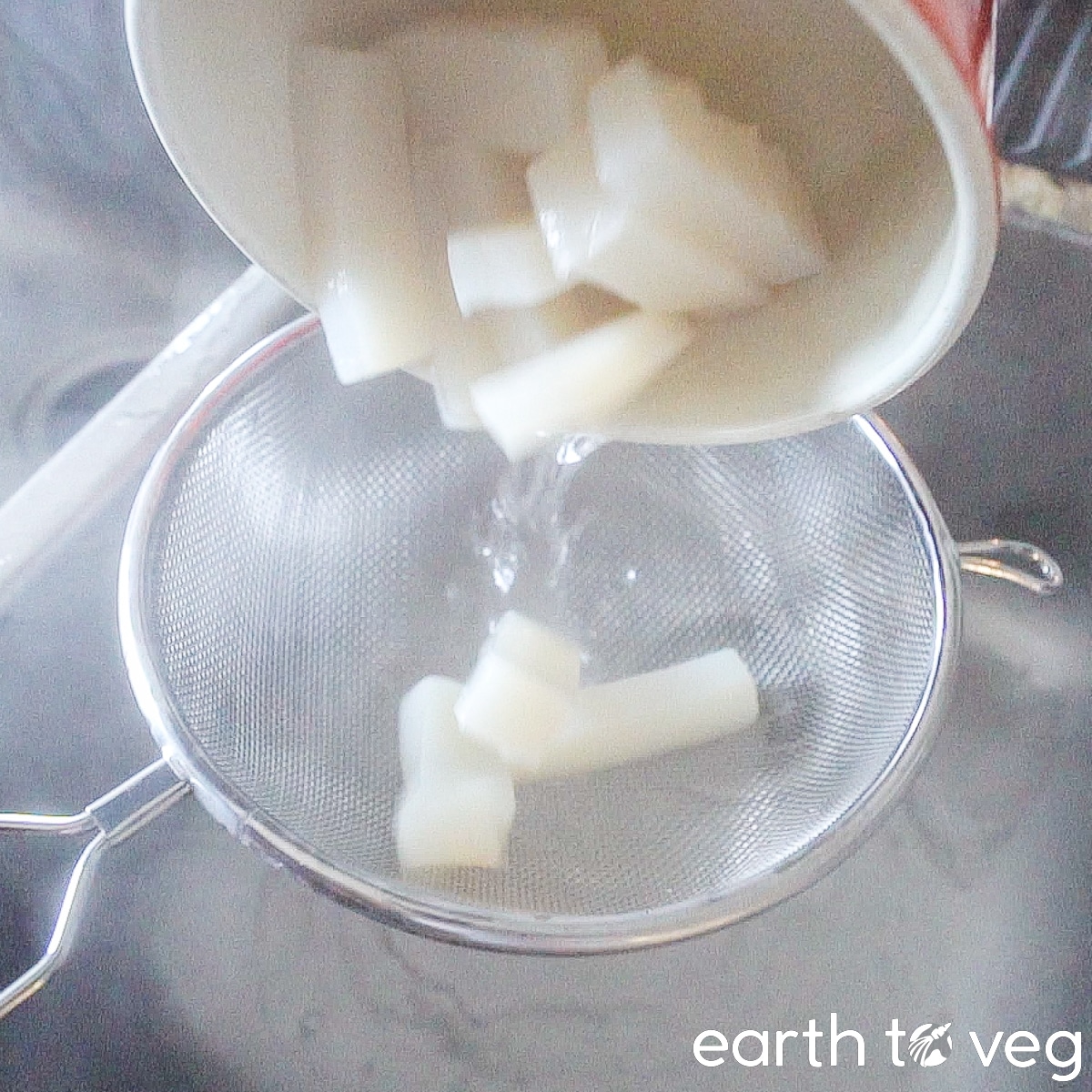 The boiled konnyaku pieces are poured into a metal strainer to drain them of water.