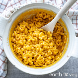 A wooden spoon sticks into a pot full of vegan mac and cheese.