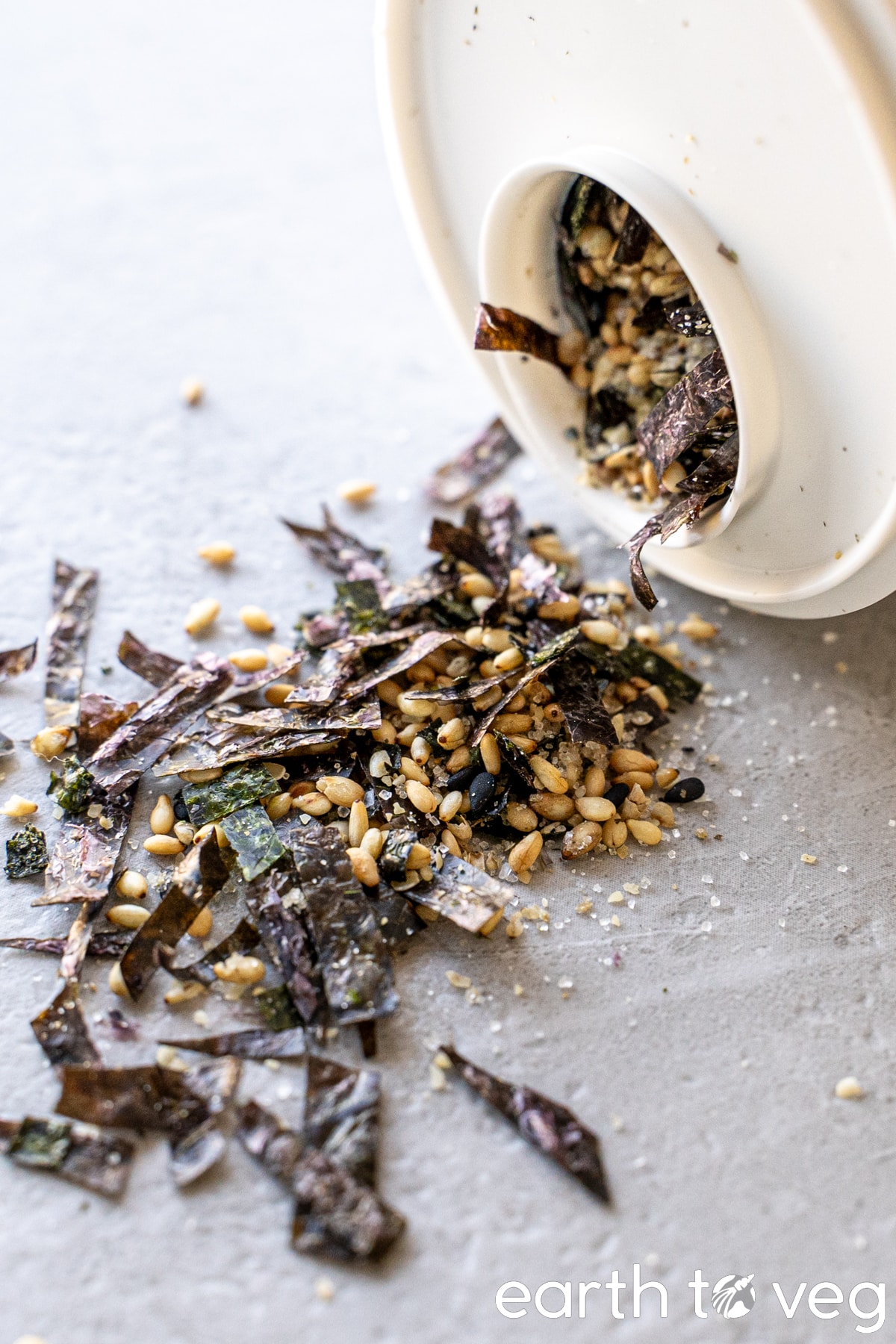 A bottle of nori komi furikake spills over a light grey surface.