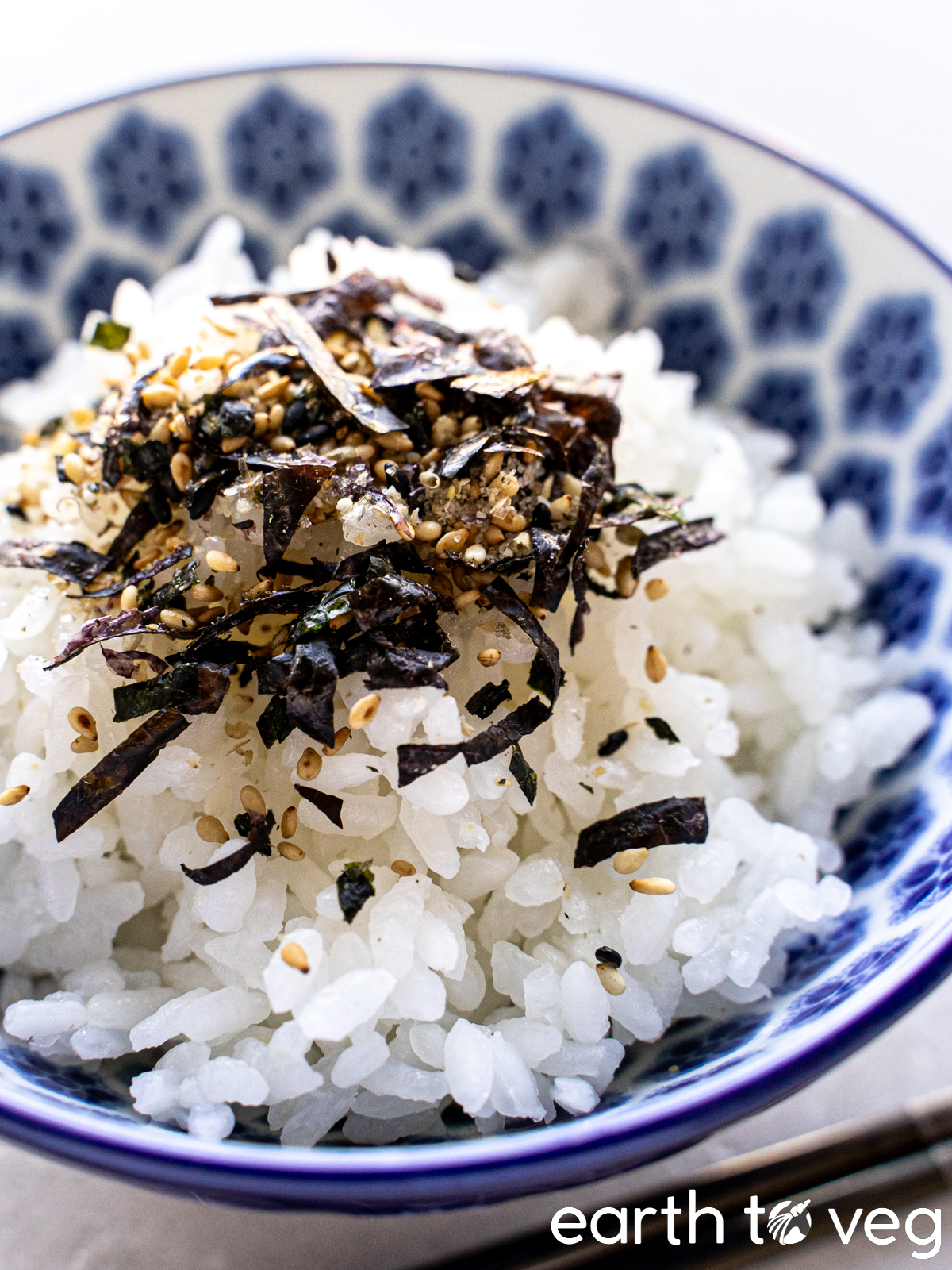 A bowl of rice in a blue china bowl is sprinkled with vegan furikake.