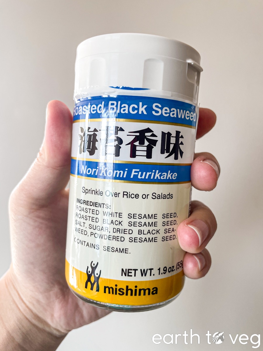 A hand holds up a small jar of Mishima brand Nori Komi Furikake.